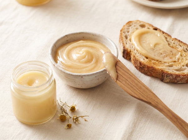 Bowl of pale whipped royal jelly honey being spread onto rustic sourdough toast