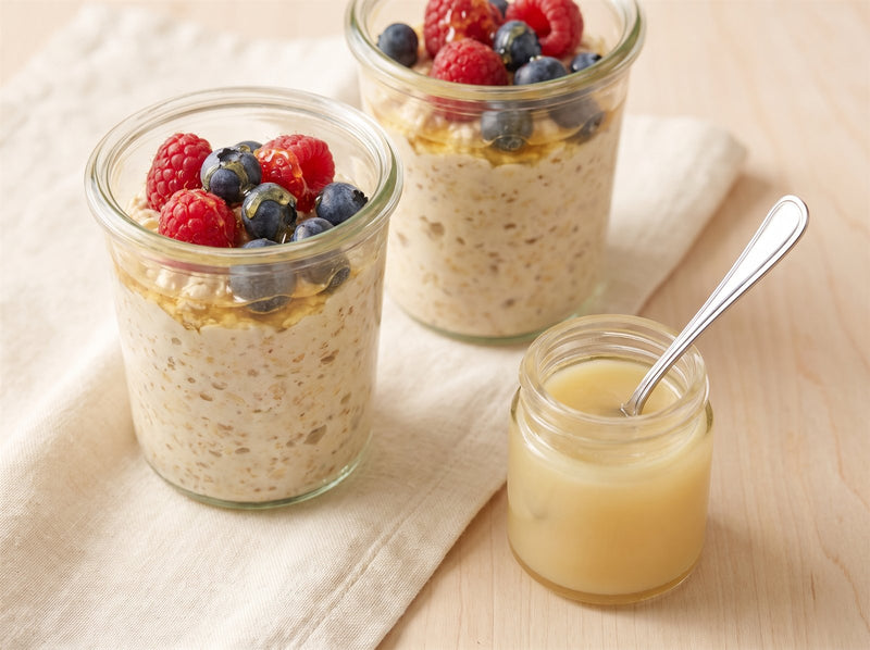 Two jars of creamy overnight oats topped with berries beside an open jar of royal jelly